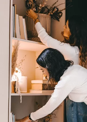 Two women tidying up a bookshelf.