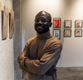 A man looking towards the camera smiling showcasing his art collection on a gallery wall.