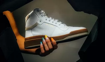 A woman's arm and hand holding a trendy pair of white sneakers.