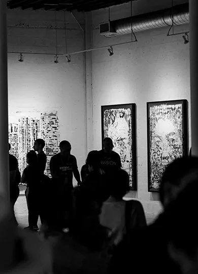 Black and white photo of people walking through an art gallery, looking at art pieces on the walls.