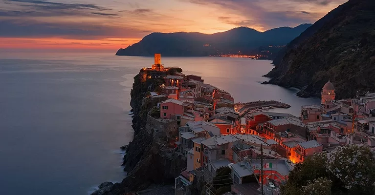 Lit up town on a cliff with a view of the sea, mountains and pink sunset