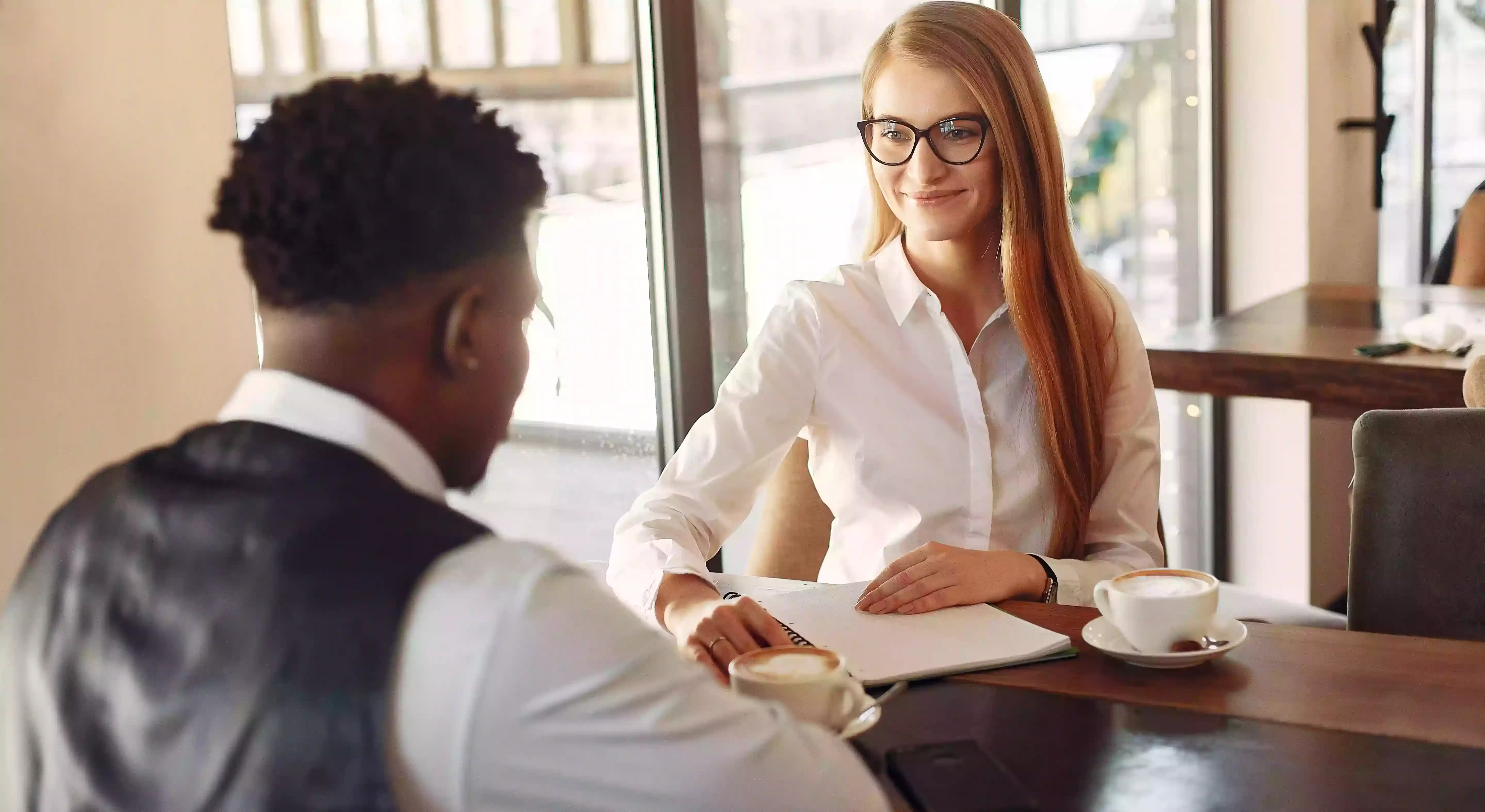 Women and man in smart clothing sat opposite each other on a table writing down on paper