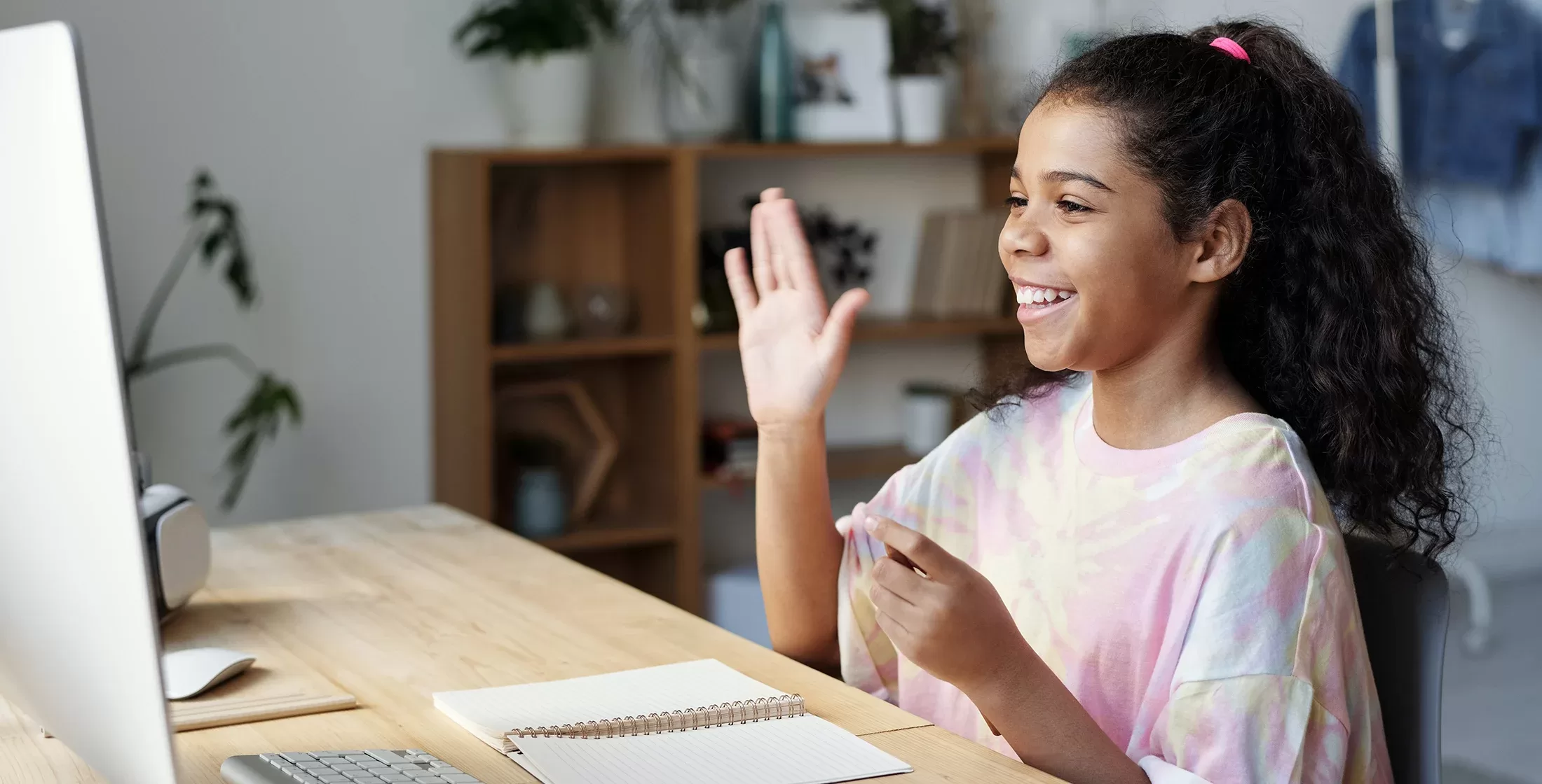Girl student sat at a desk smiling at her MacBook with one hand in the air