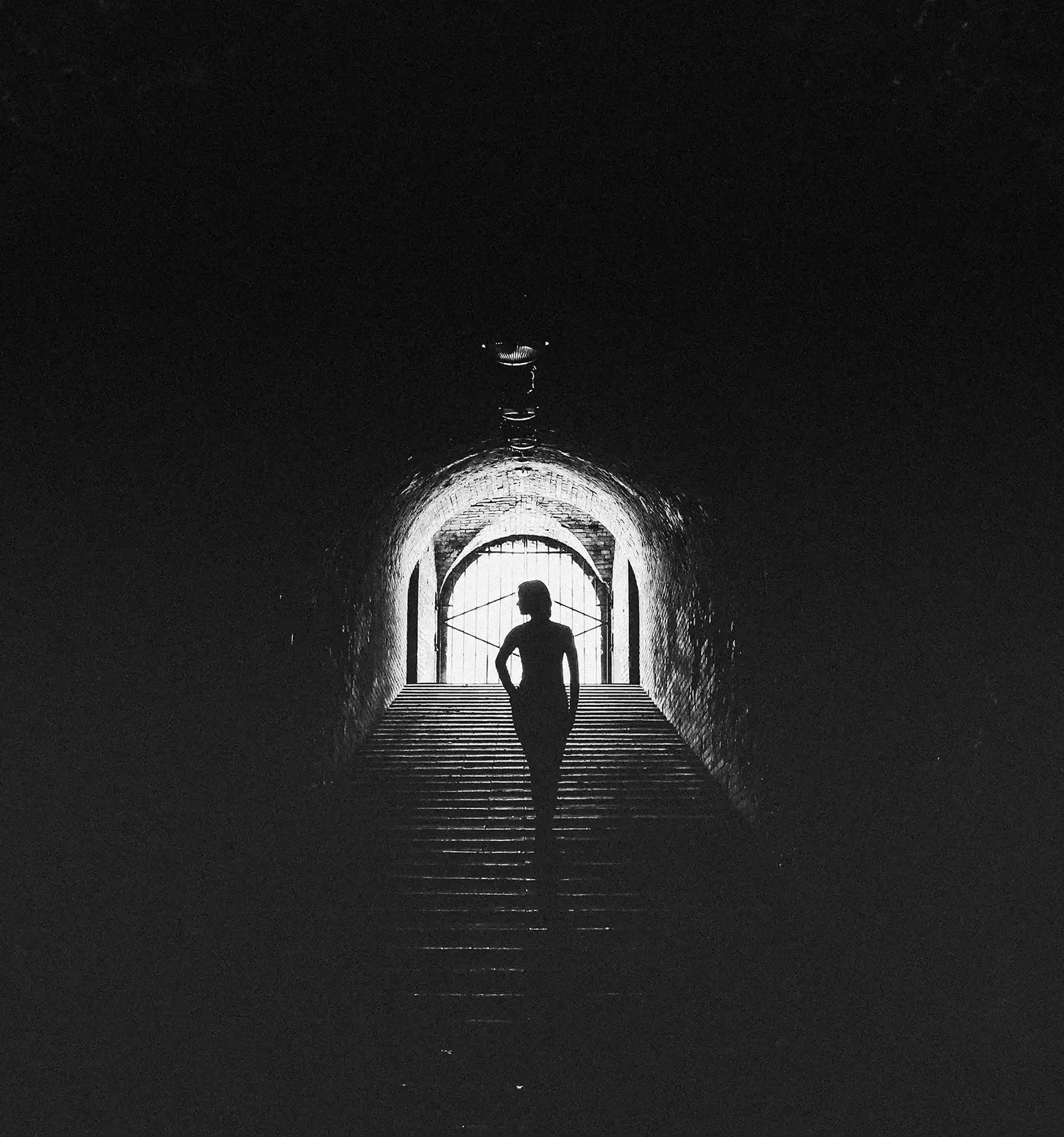 Black and white photo of a female silhouette walking up the stairs of an underground walkway