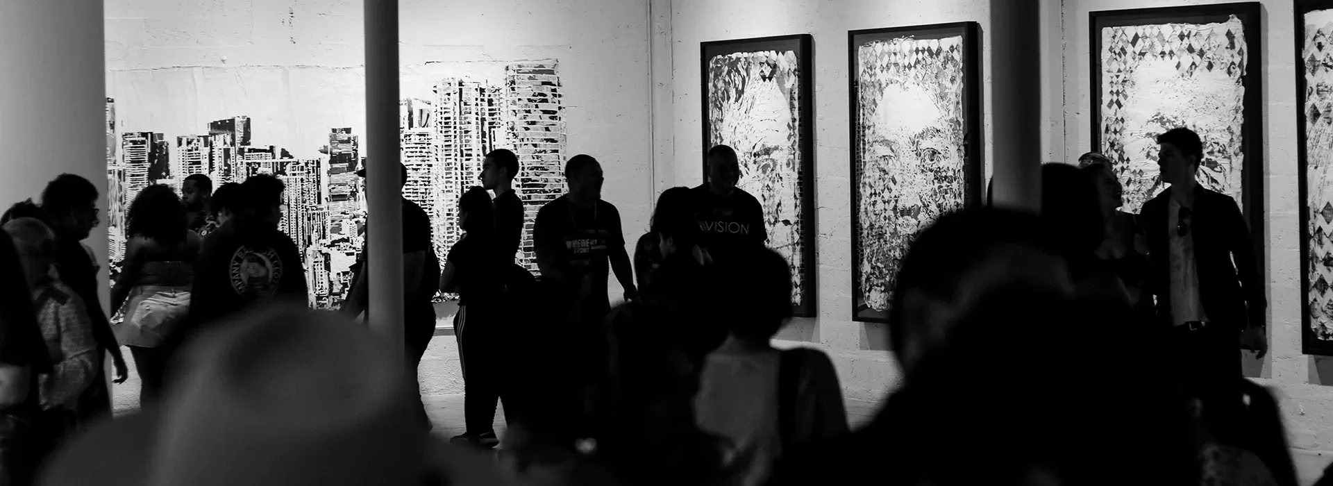 Black and white photo of people walking through an art gallery, looking at art pieces on the walls.