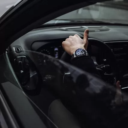 Close up of hand wearing a watch over steering wheel of car through the window.