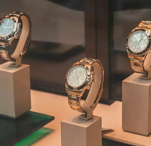 Luxury watches displayed on stands in a well-lit store, showcasing their intricate dials and metallic bands. The watches have a classic design, with a focus on elegance and precision.
