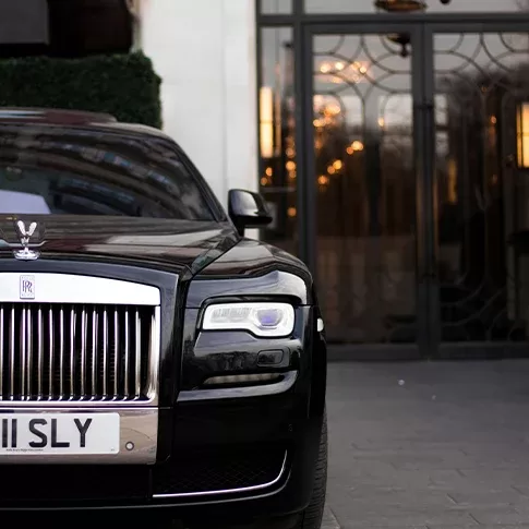 A black stunning shiny Rolls Royce with silver wheels parked outside a fancy hotel.
