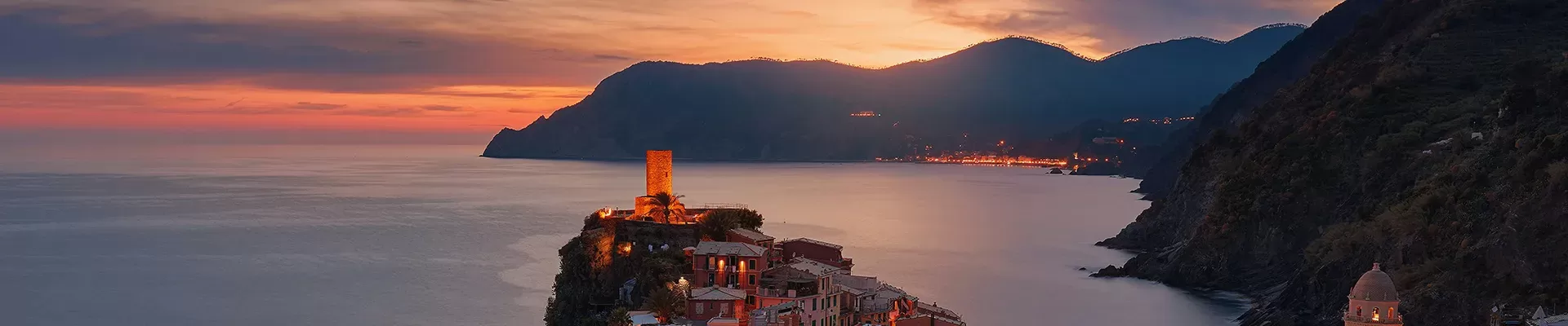 Lit up town on a cliff with a view of the sea, mountains and pink sunset