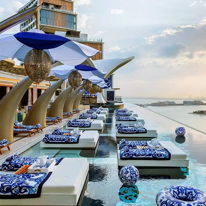 Sun lounger white beds on top of infinity pool overlooking Dubai sea and view. The sunbeds have navy and white beautiful patterns on it that match the lamps and beach balls in the pool.