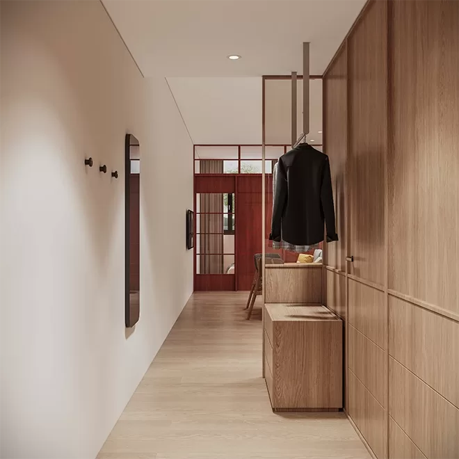 Minimalist hallway with light wood floors and walls, featuring a sleek black coat on a hanger, wooden cabinets lining the side, a wall mirror, and a glimpse into a room with red-framed glass doors at Alma House, Singapore.