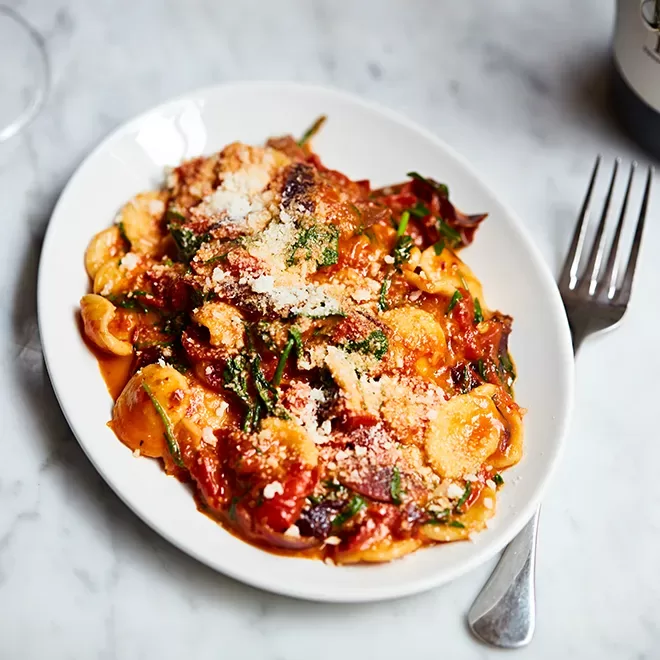 A plate of orecchiette pasta topped with tomato sauce, spinach, and grated parmesan cheese. A fork is placed to the right of the dish on a marble surface at Bocca di Lupo, Soho, London.