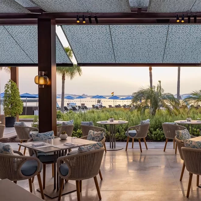 Light and bright open windowed room with tables and chairs overlooking sea front.