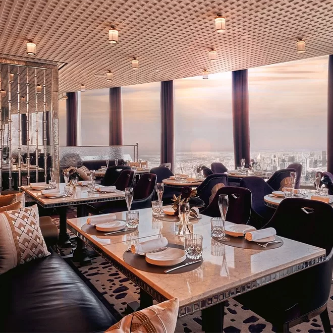 Beautiful restaurant with tables laid out overlooking the view of Dubai over the sea.