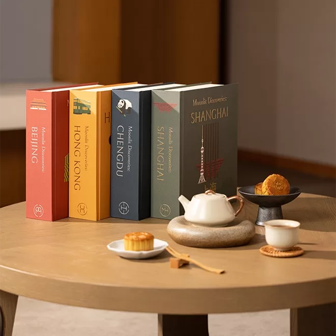 A variety of boxes of mooncakes are displayed on a coffee table next to a small plate of mooncakes and tea cup and saucer.