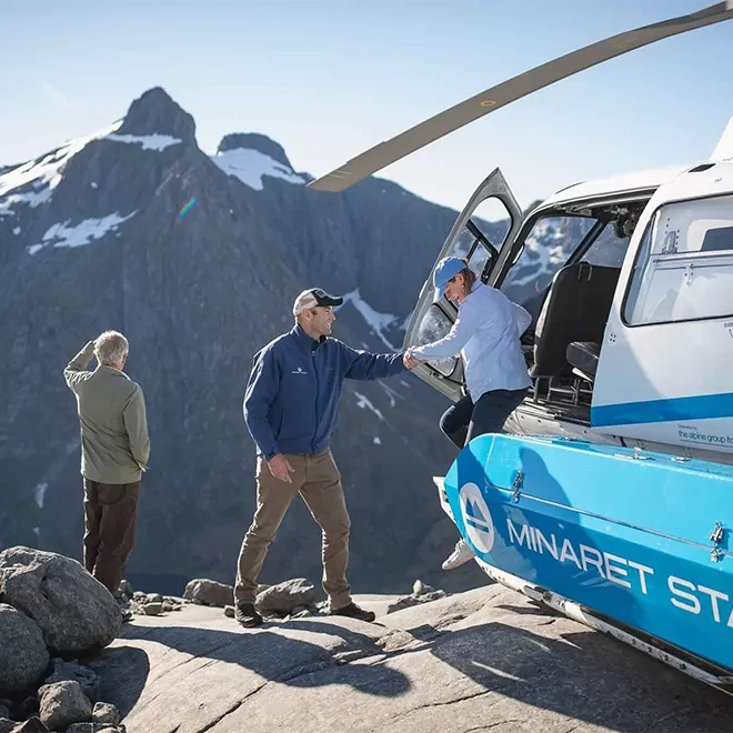 Man helping women to get out of helicopter whilst another person looks out to mountainous view at Minaret Station Alpine Lodge, New Zealand.