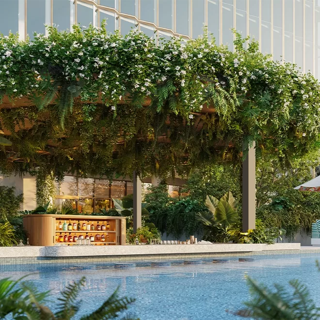 A luxurious outdoor bar with a lush green canopy and hanging plants overlooks a sparkling pool. Bottles are arranged on the bar counter, and the setting is surrounded by greenery beneath a modern building with glass windows at The Standard, Singapore.