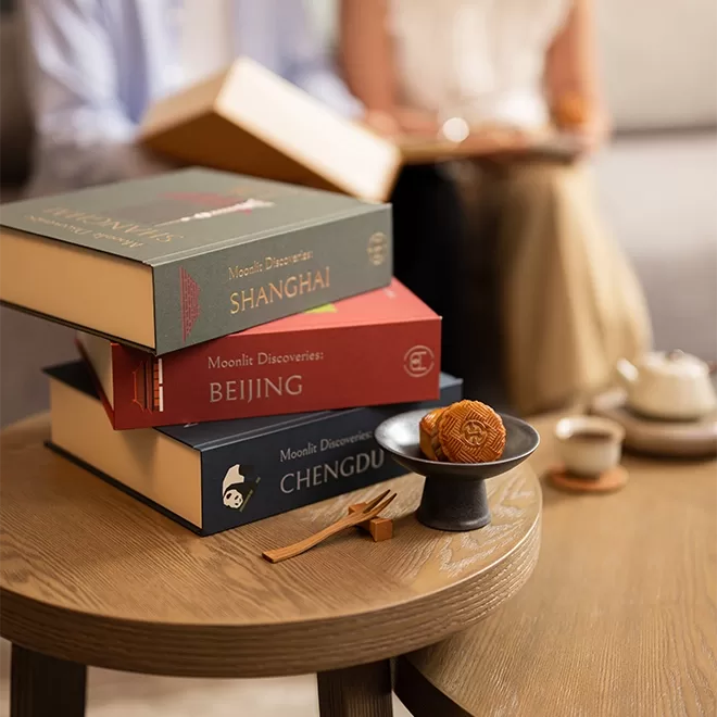 A variety of boxes of mooncakes displayed on a coffee table next to a small plate of mooncakes in front of a couple sat on a sofa at The Upper House, Hong Kong.