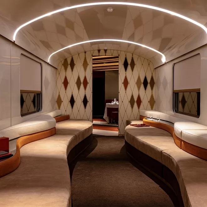 Luxurious train carriage of La Dolce Vita Orient Express in Italy. Its interior with curved, upholstered seating along both sides. The walls feature a diamond pattern, and soft lighting arches across the ceiling, enhancing the elegant atmosphere. .