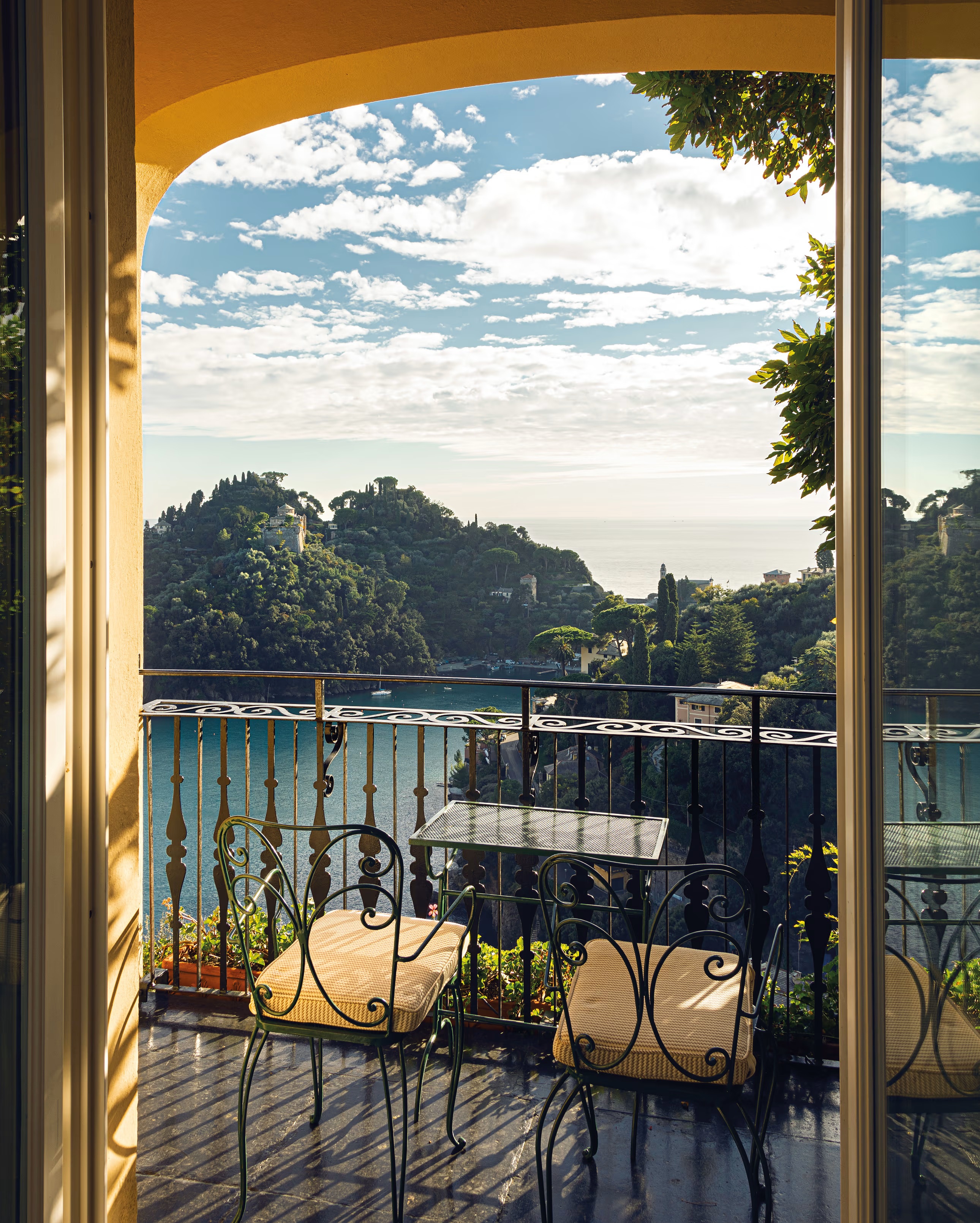 Balcony of two green abstract design garden chairs with cushions  with a view of lake and trees.
