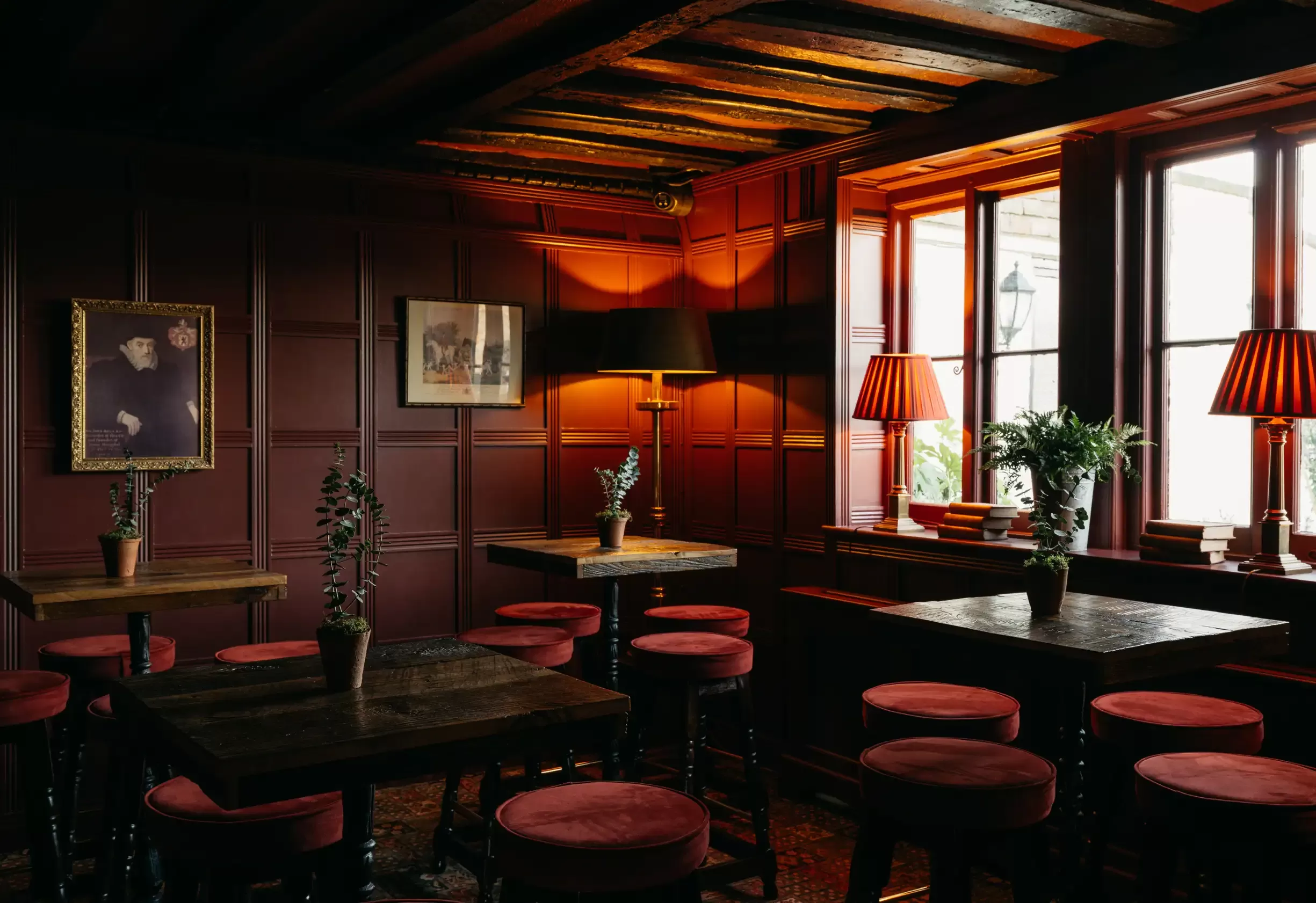 Maroon walls, red velvet stools and wooden tables with red dim light interior at Boys Hall, Ashford
