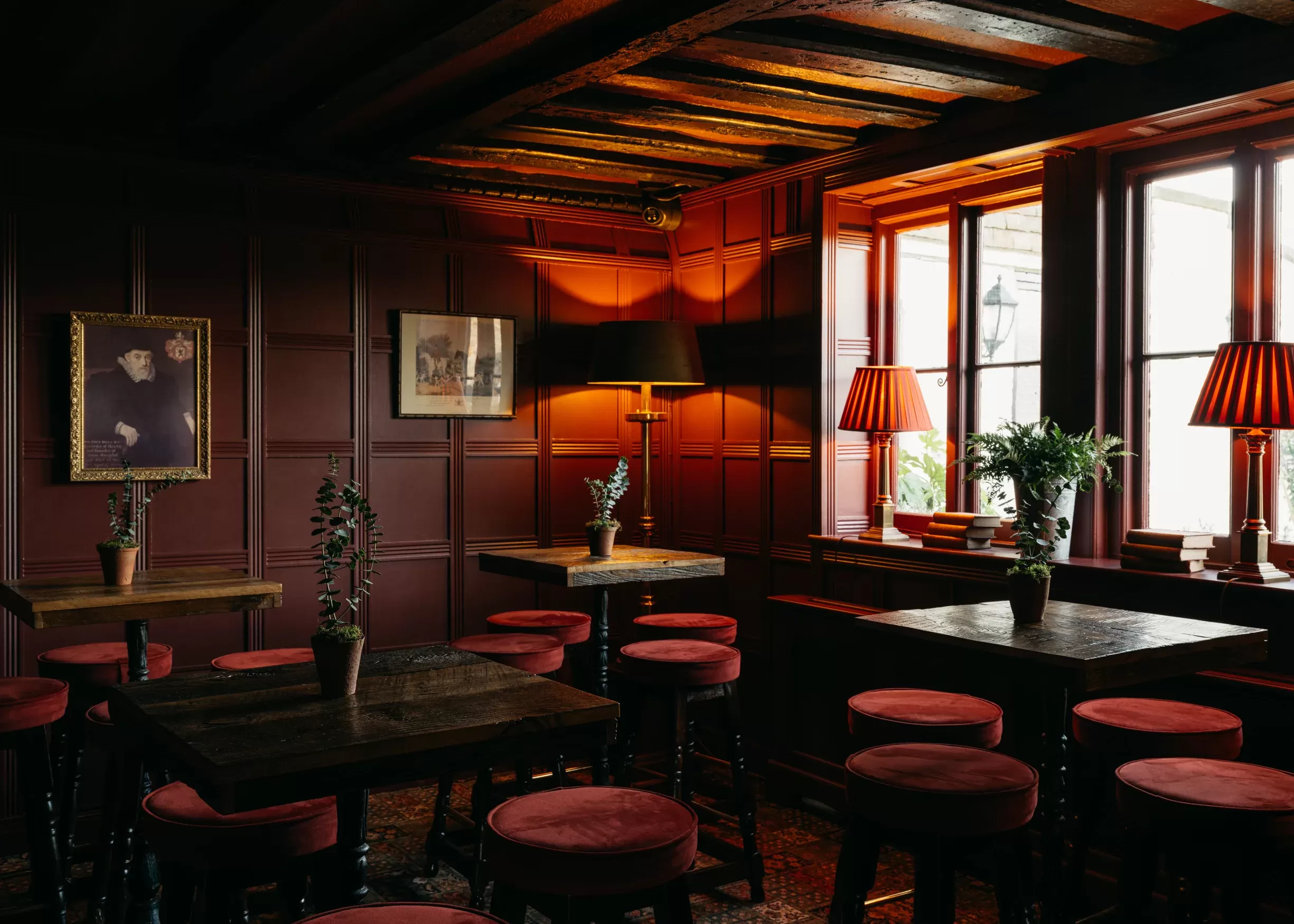 Maroon walls, red velvet stools and wooden tables with red dim light interior at Boys Hall, Ashford