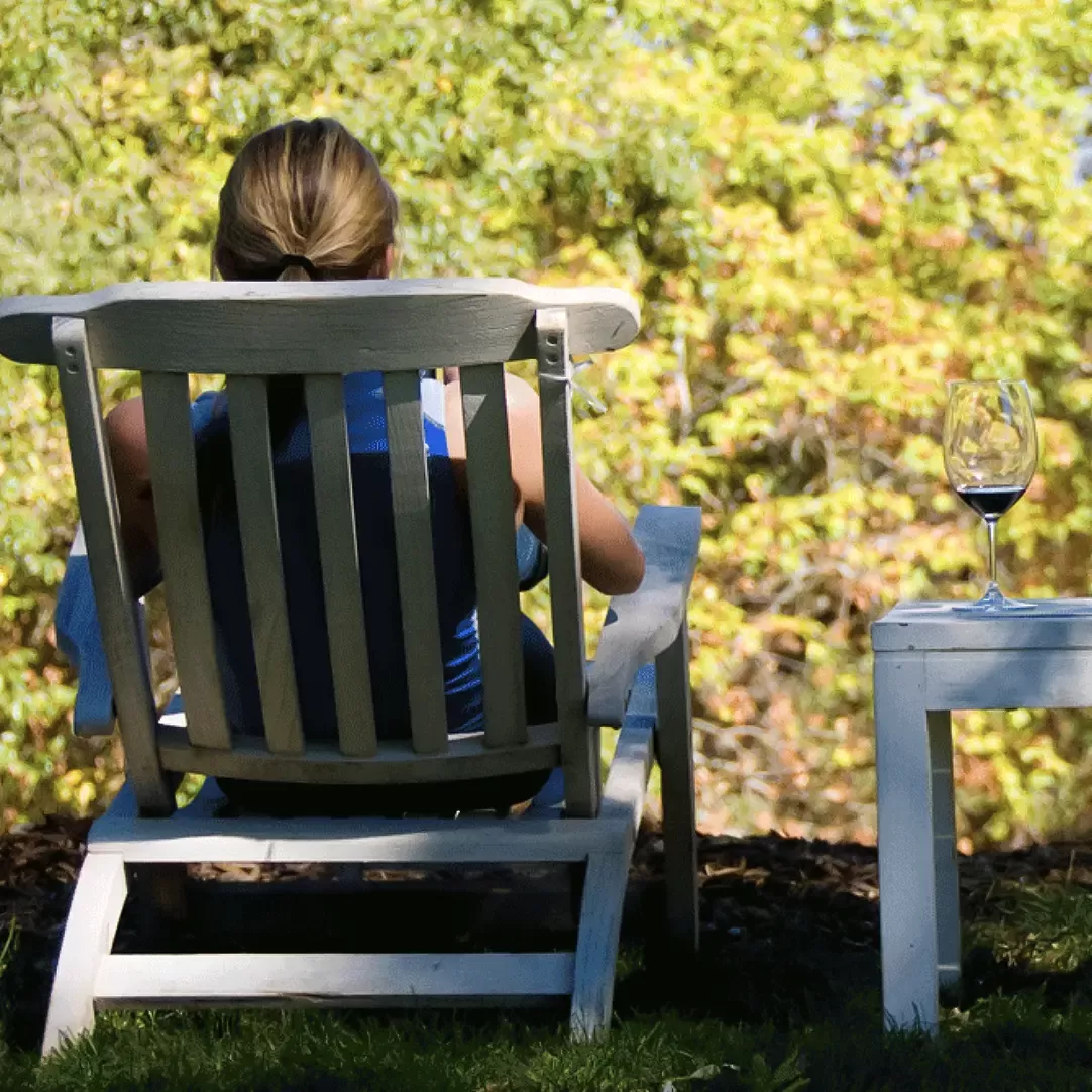 Women sat on a low garden chair with a glass of red wine in the sun looking at trees