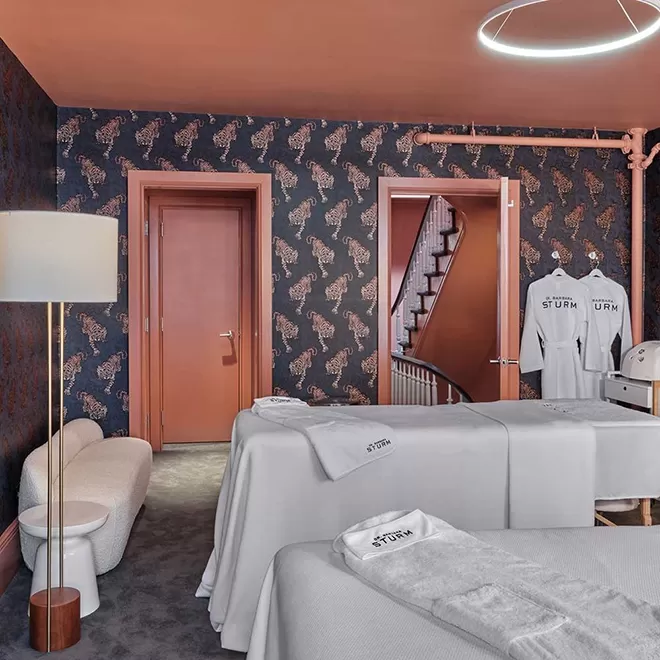 Luxury spa treatment room with treatment bed, robes and seating area with tiger-printed wallpaper interior at Dr Barbara Sturm Madison Ave NYC Spa & Boutique, New York