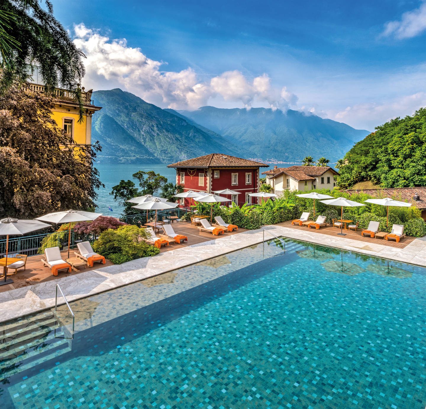 Outside luxury Grand Hotel Tremazzo pool and orange sunbeds and pool house on the Lake overlooking mountains,