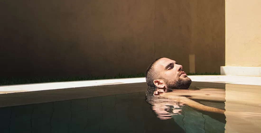 Man in swimming pool leading head on side of the pool in a spa
