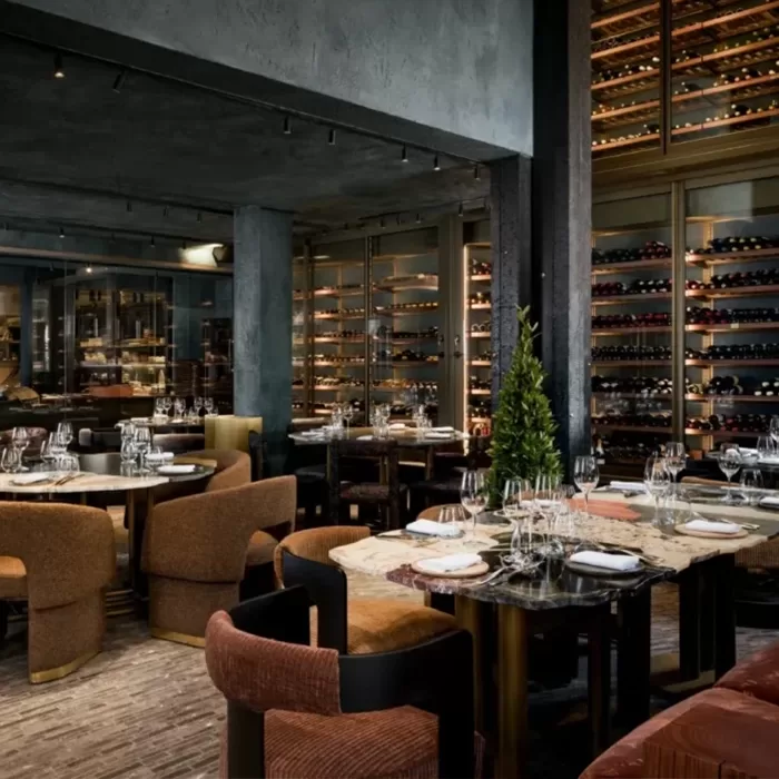 A modern, upscale restaurant with elegant tables set for dining, plush chairs, and shelves filled with wine bottles along the walls, creating a sophisticated and inviting atmosphere.