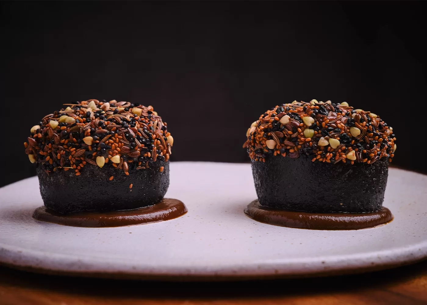 Two pieces of cuttlefish bun, heritage seeds, and black garlic served on a white plate at AngloThai in London.