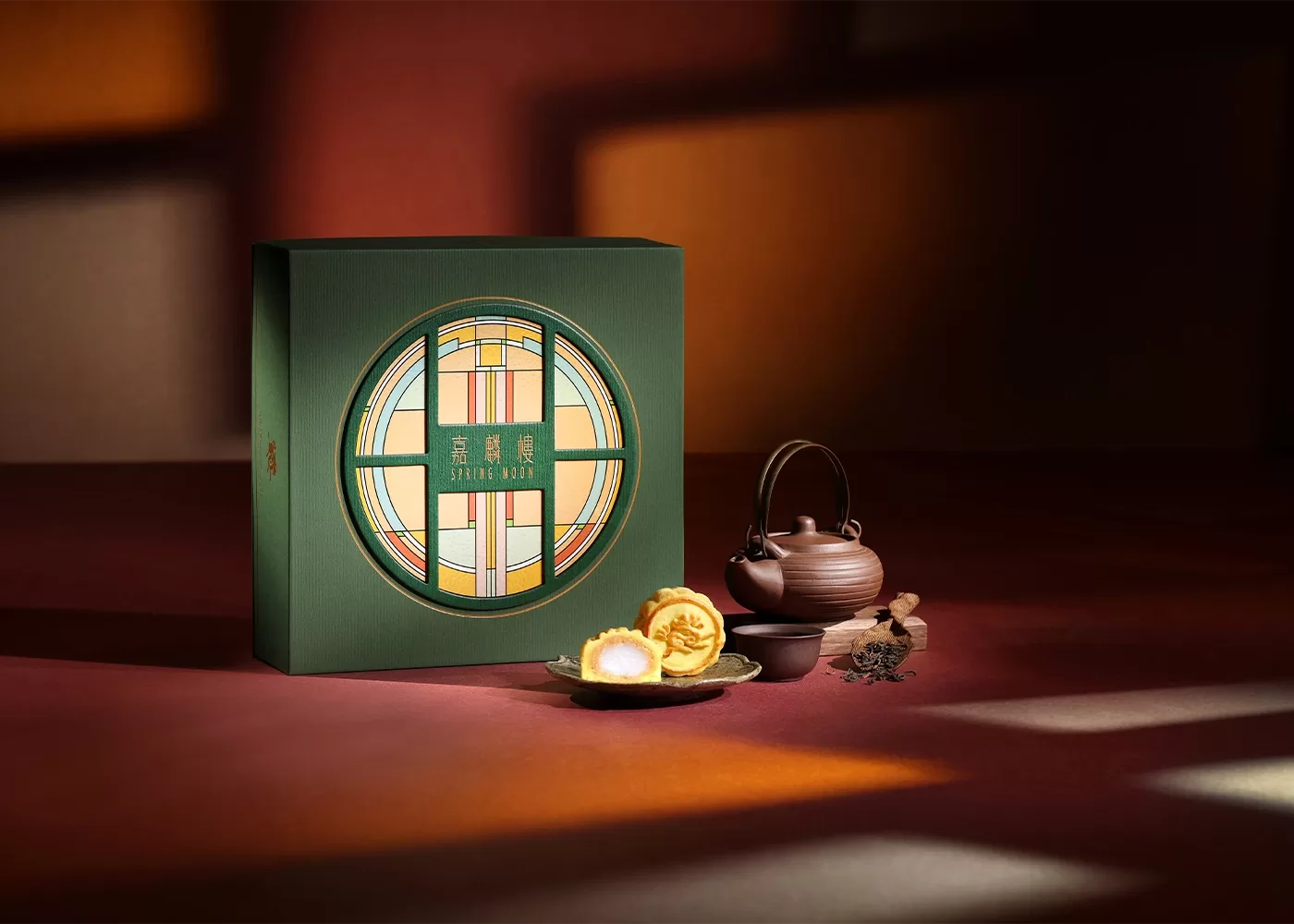 A small plate of two limited Edition Sesame Paste Mochi Mooncakes is displayed on an organised scene with a decorated assortment box, teacup, and saucer at The Peninsula Hong Kong.