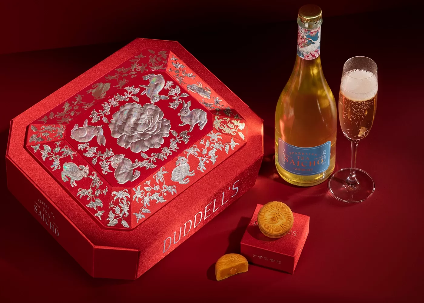 Duddells mooncake served on a red velvet box next to a red decorated assortment box and a bottle and glass of champagne, Hong Kong.