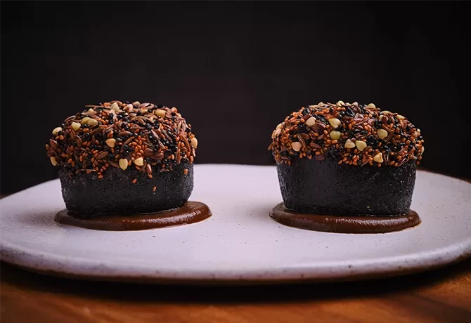Two pieces of cuttlefish bun, heritage seeds, and black garlic served on a white plate at AngloThai in London.