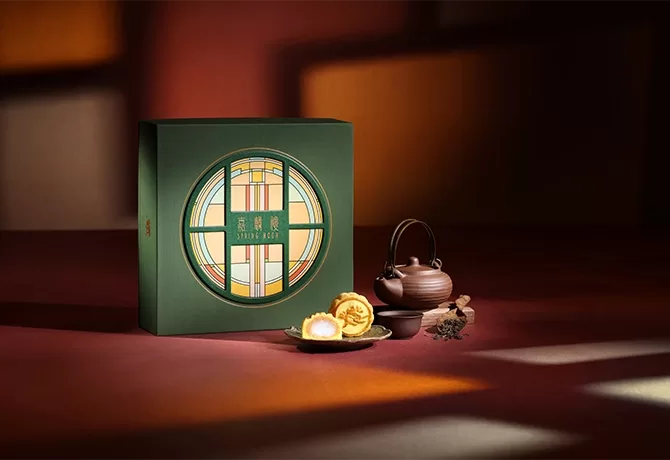 A small plate of two limited Edition Sesame Paste Mochi Mooncakes is displayed on an organised scene with a decorated assortment box, teacup, and saucer at The Peninsula Hong Kong.