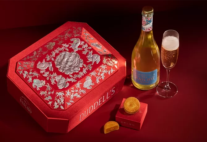 Duddells mooncake served on a red velvet box next to a red decorated assortment box and a bottle and glass of champagne, Hong Kong.