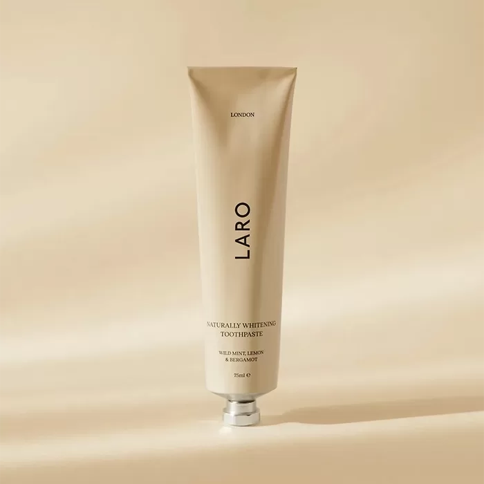 A tube of LARO Naturally Whitening Toothpaste stands upright on a beige surface. The packaging is sleek and minimalist, with black text and a small amount of shadow cast on the background.