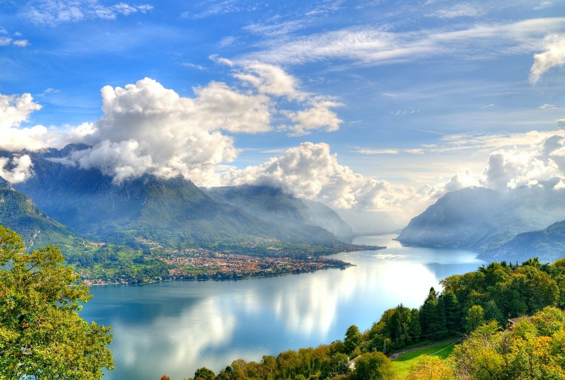 View of winding Lake Como between mountains covered in clouds and view of town