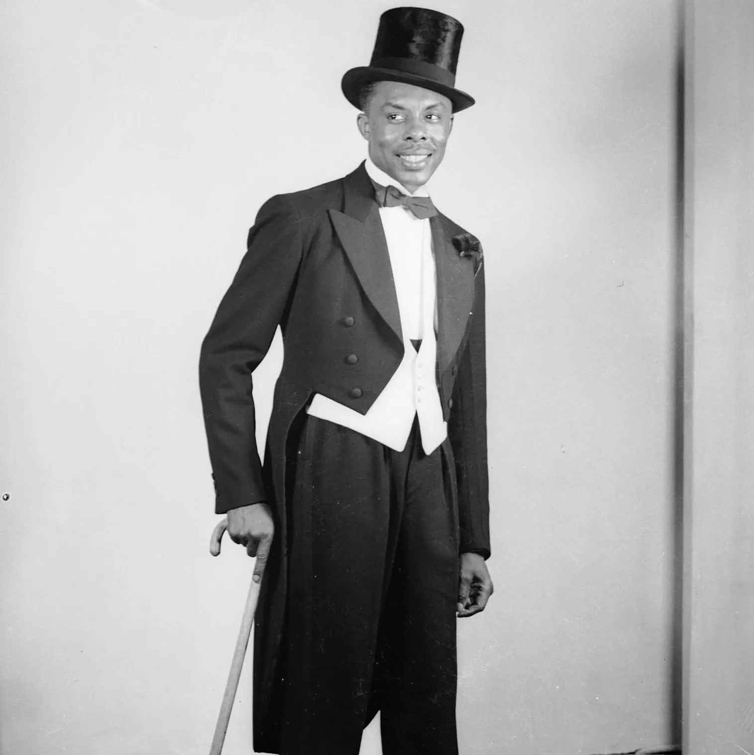 Black and white photo of man wearing formalwear with walking stick and opera hat
