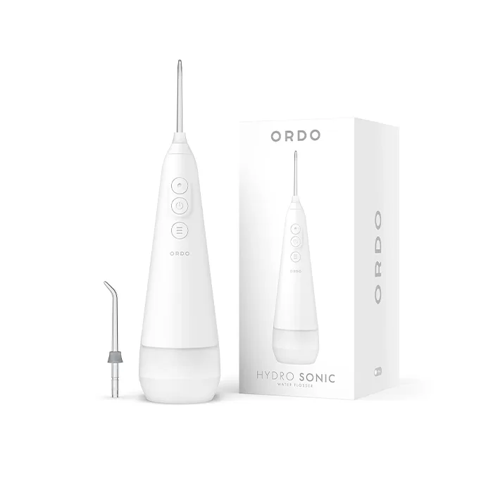 A white Ordo Hydro Sonic water flosser stands beside its box. The device features a sleek design with buttons on its front and comes with a detachable nozzle. Both the product and the box display the Ordo branding.