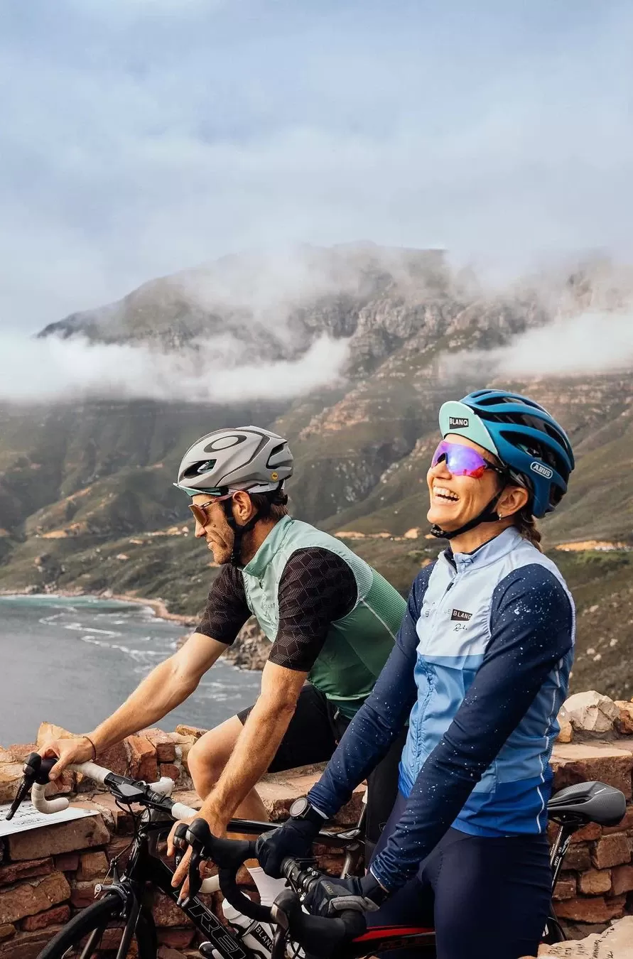 Man and women in cycling gear smiling riding bikes overlooking mountain and sea landscape in Norway