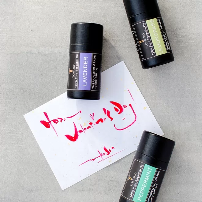 Three tubes of essential oil (lavender, lemongrass, and peppermint) are arranged around a handwritten card that says Happy Valentines Day! with a heart and smiley face.