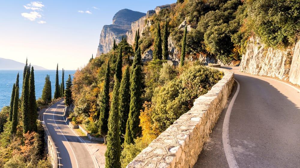 Highway roads up mountain with cobbled stone barriers surrounded by trees overlooking the sea
