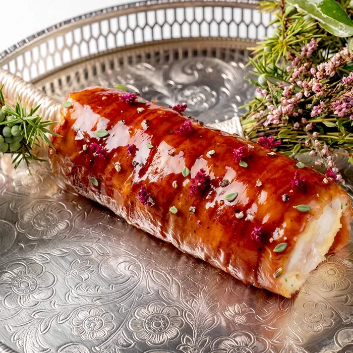 A beautifully presented dish featuring a glazed, rolled piece of lobster on an intricate silver platter. Its garnished with herbs and small flowers, adding a decorative touch. A sprig of greenery lies beside it on the tray, served at Alex Dilling at Hotel Café Royal, Piccadilly in London.