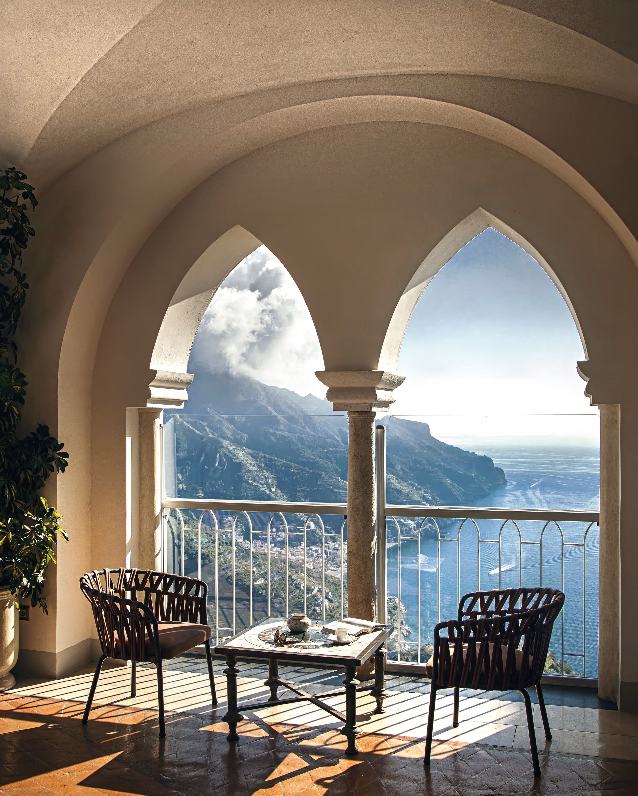 2 chairs and low squares table underneath double archway overlooking coast and mountains