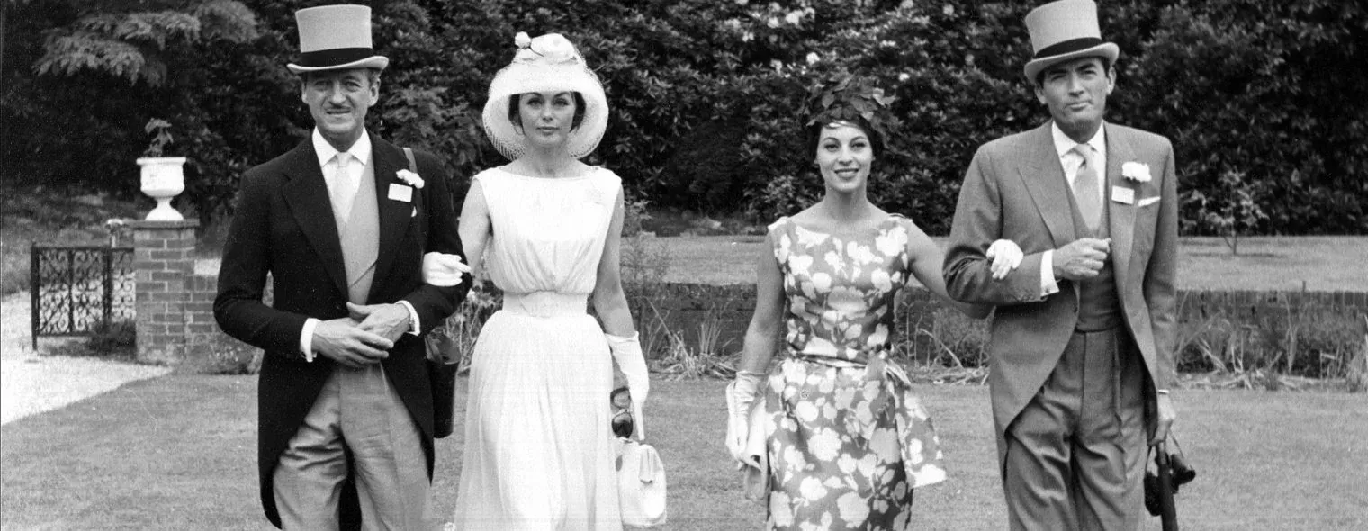 Vintage black and white photo of two couples wearing dresses and morning dress walking through park