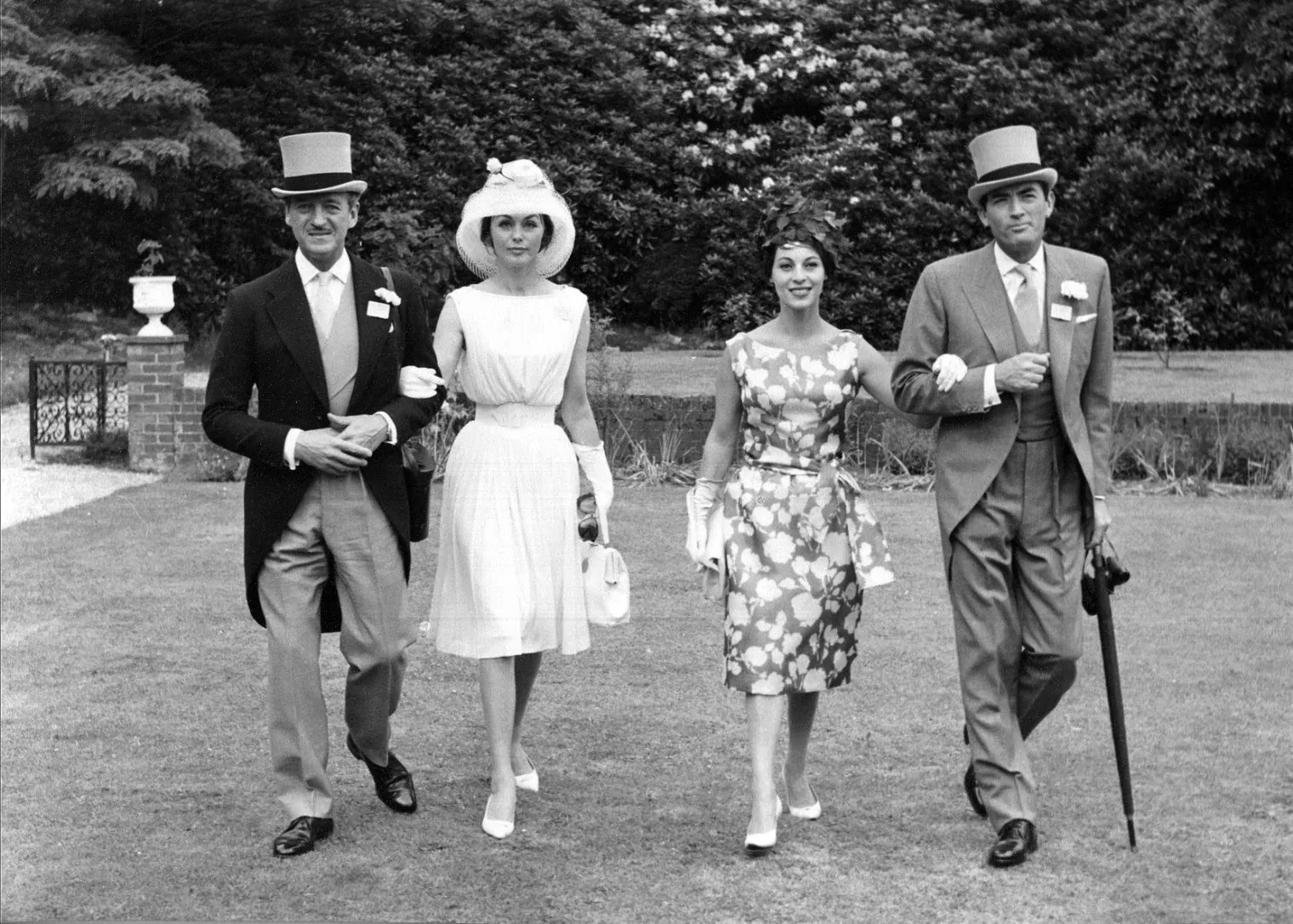 Vintage black and white photo of two couples wearing dresses and morning dress walking through park