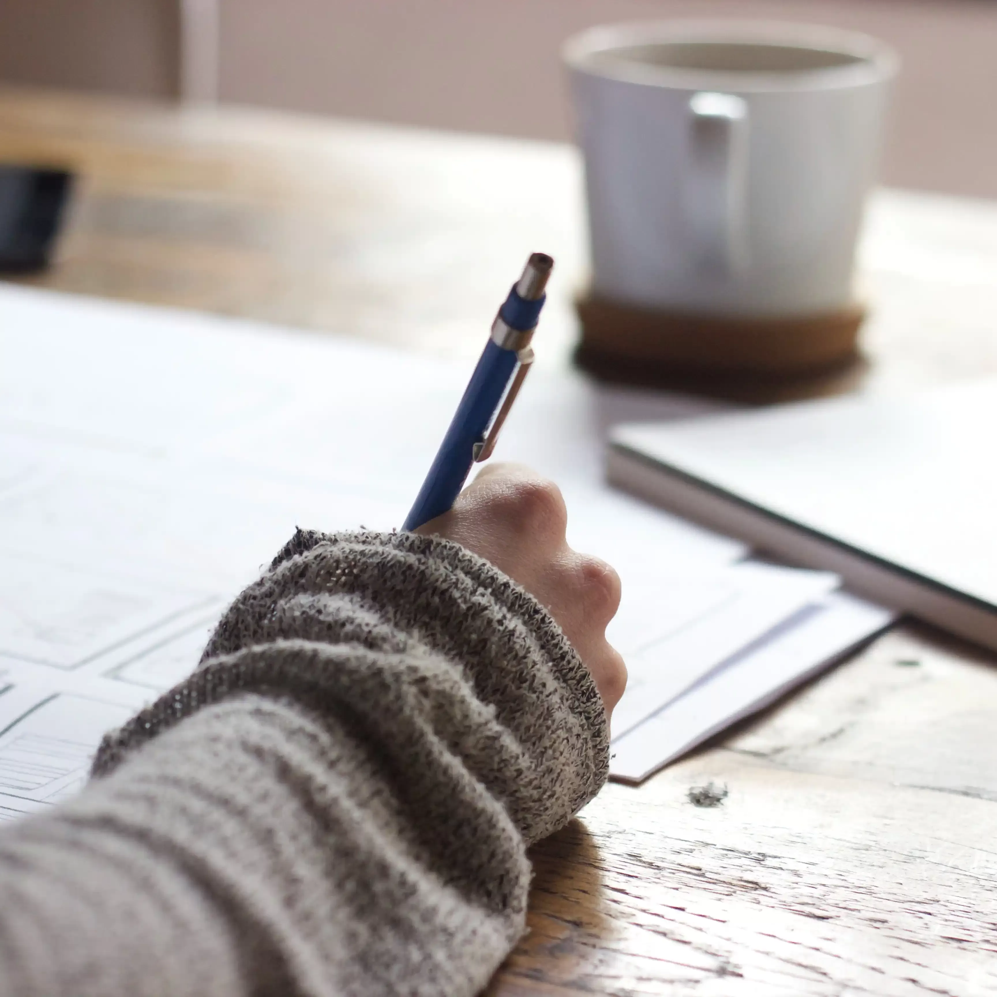 Person writing in a book on a wooden table with a coffee