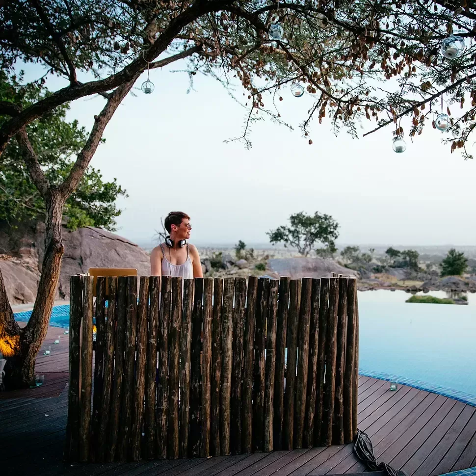 A DJ poolside spinning decks behind a bamboo table.
